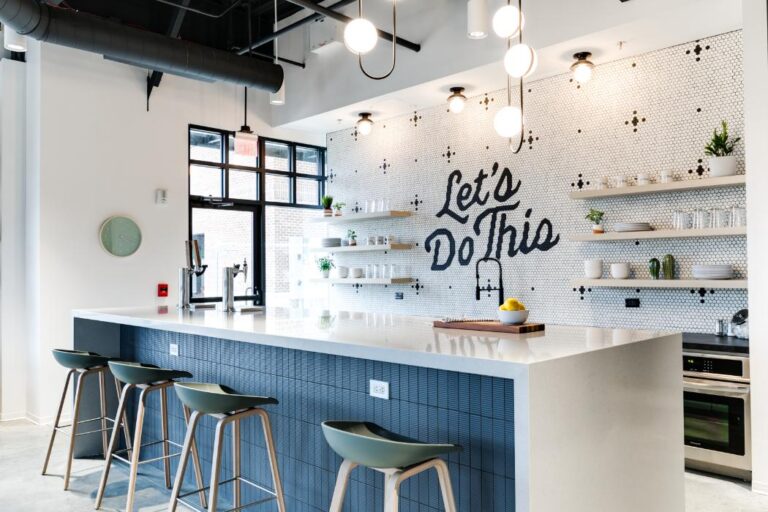 Modern kitchen with a large white island, green stools, and open shelves. The wall reads "Let's Do This" in bold text, conveying motivation and energy.