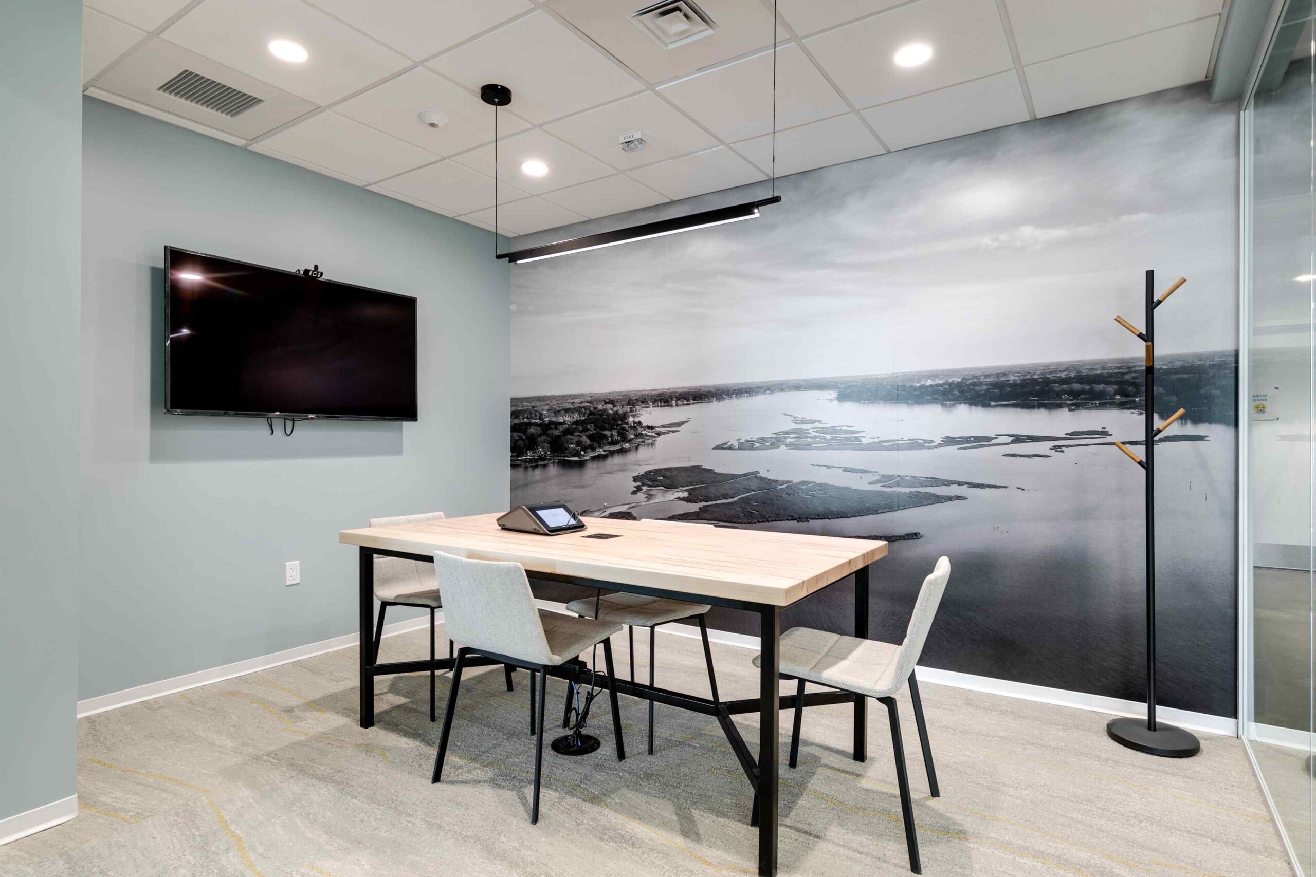 Modern Gather team suite with a light wood table, gray chairs, and a mounted TV. A large abstract black and white mural enhances the space.
