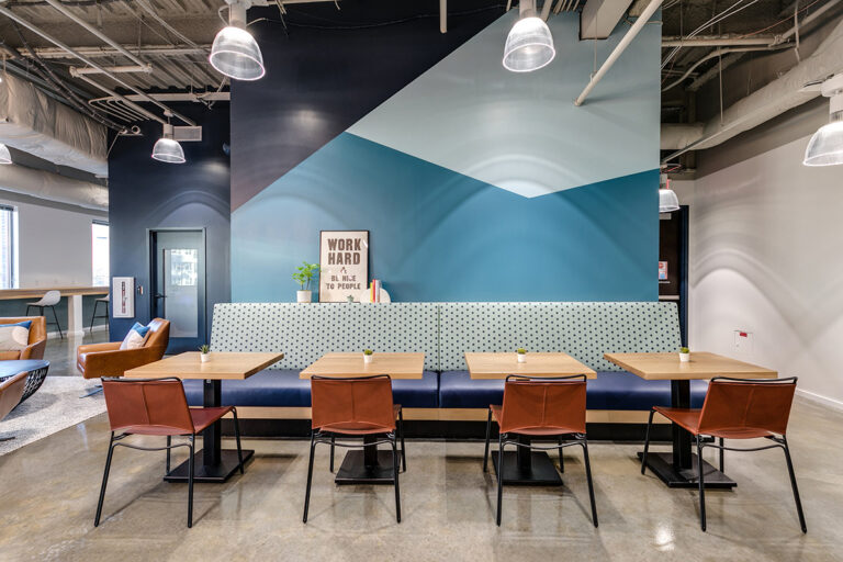 Newport News, VA Modern office lounge with blue geometric wall, pendant lights, and brown leather chairs at wooden tables. "Work hard" sign adds motivational touch.