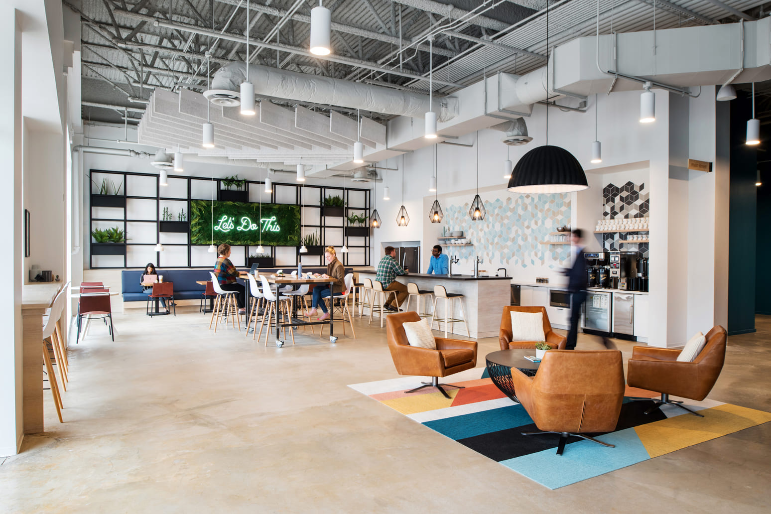 Bright Gather coworking space with kitchen bar, communal worktables, and lounge seating under a high industrial ceiling.