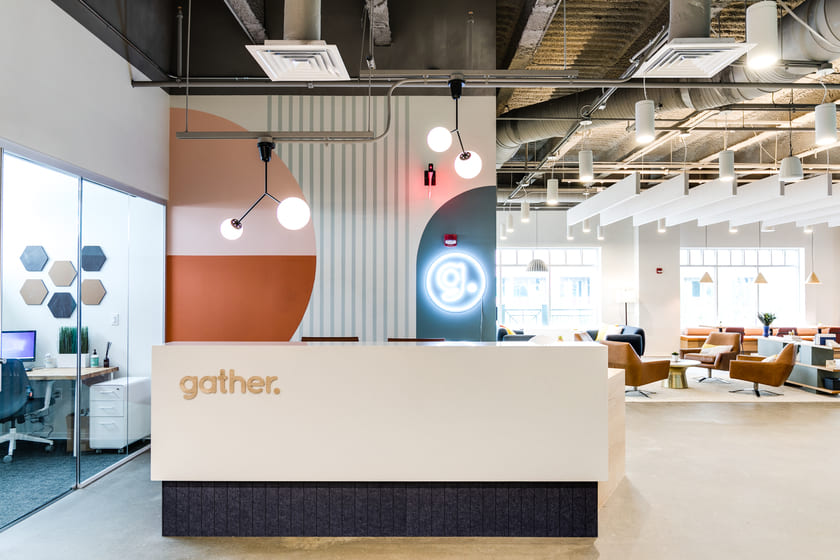 Gather coworking reception area with branded front desk, modern pendant lighting, and an open lounge workspace in the background.