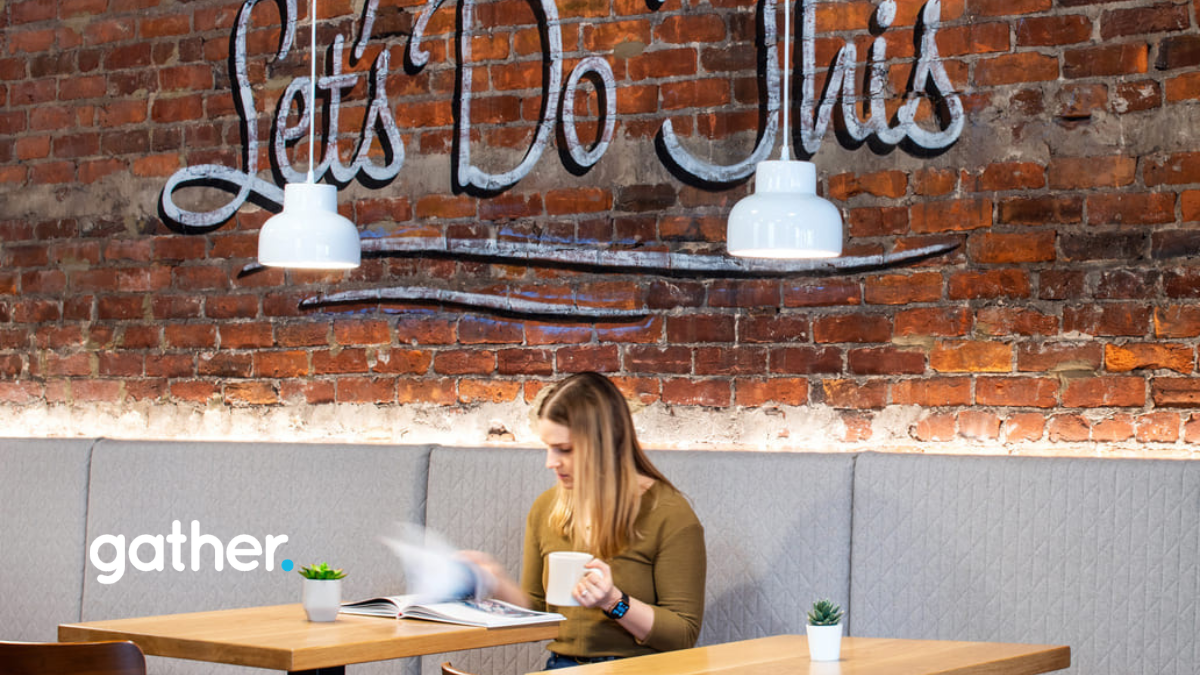 Woman sitting at a table at Gather Workspaces reading in front of a wall of exposed brick