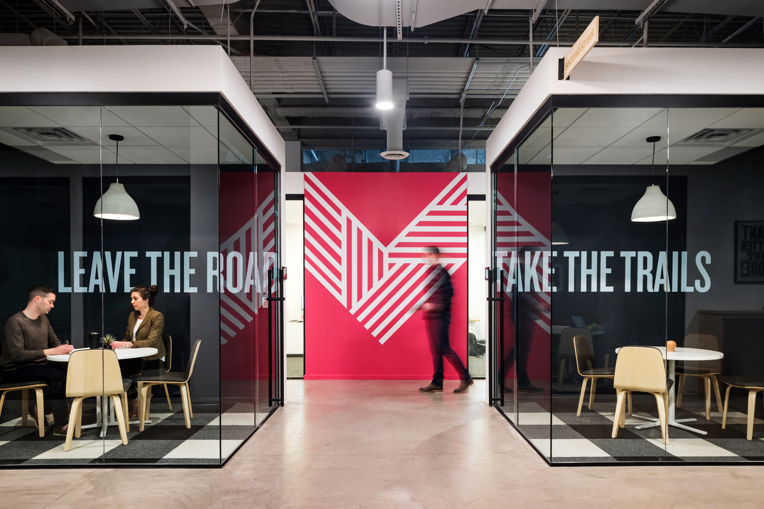 Glass-walled conference rooms at Gather Workspaces with “Leave the Road” and “Take the Trails” lettering
