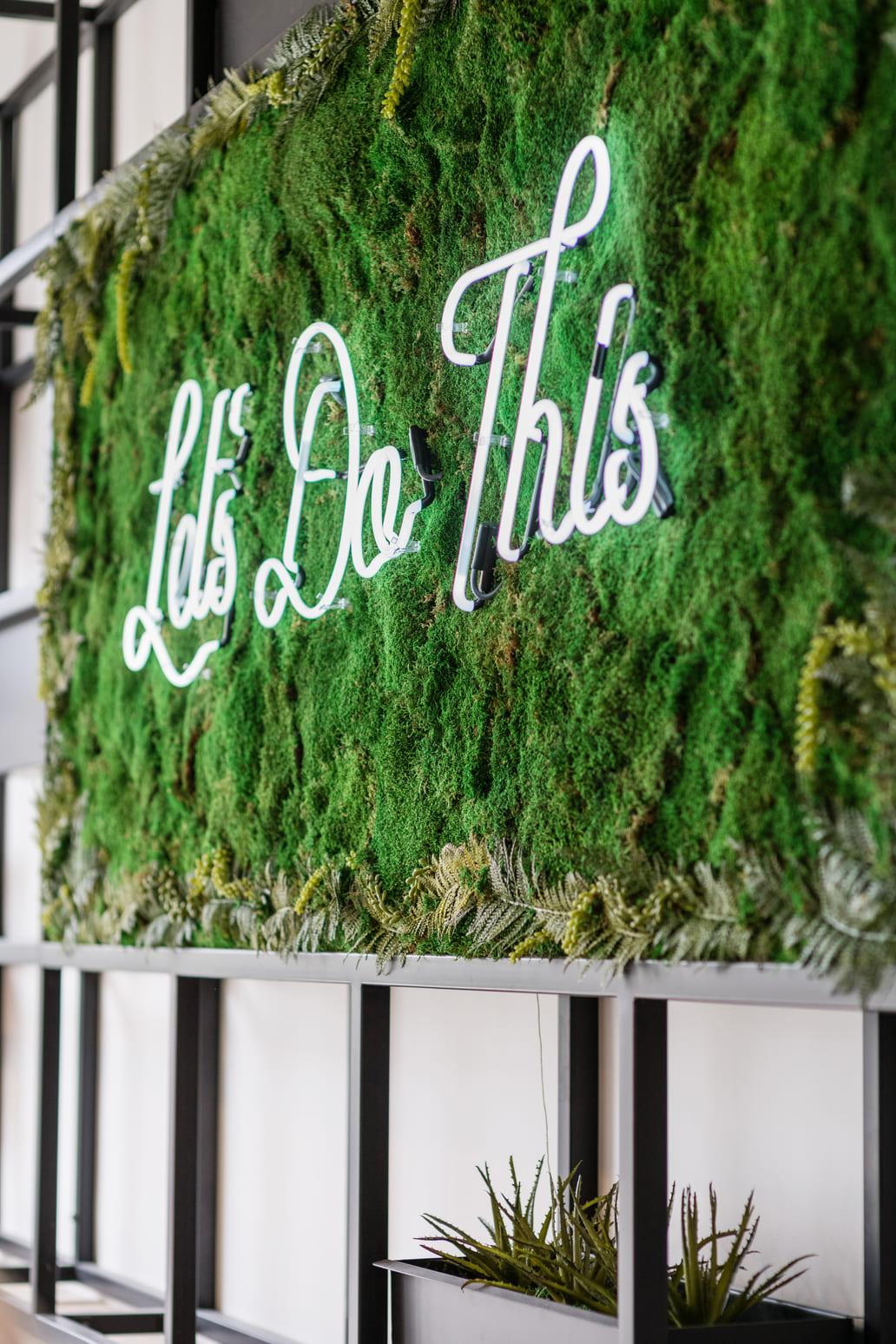 Let’s Do This” neon sign on a green moss wall inside Gather Workspaces