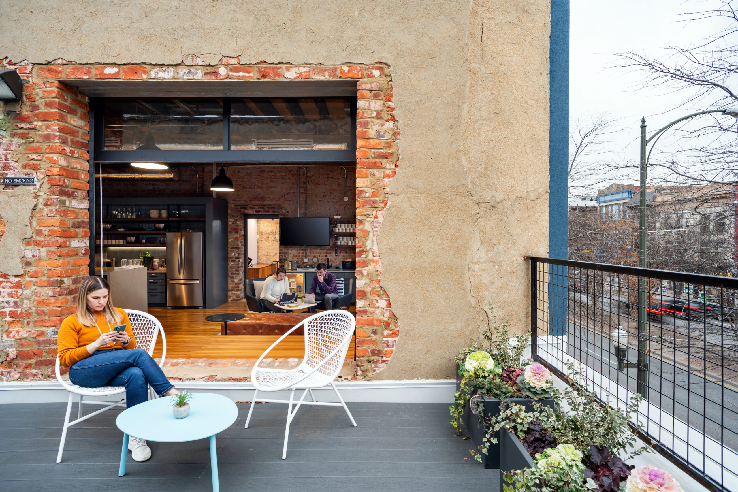 Outdoor patio workspace at Gather Arts District with exposed brick, modern seating, and view into coworking kitchen area