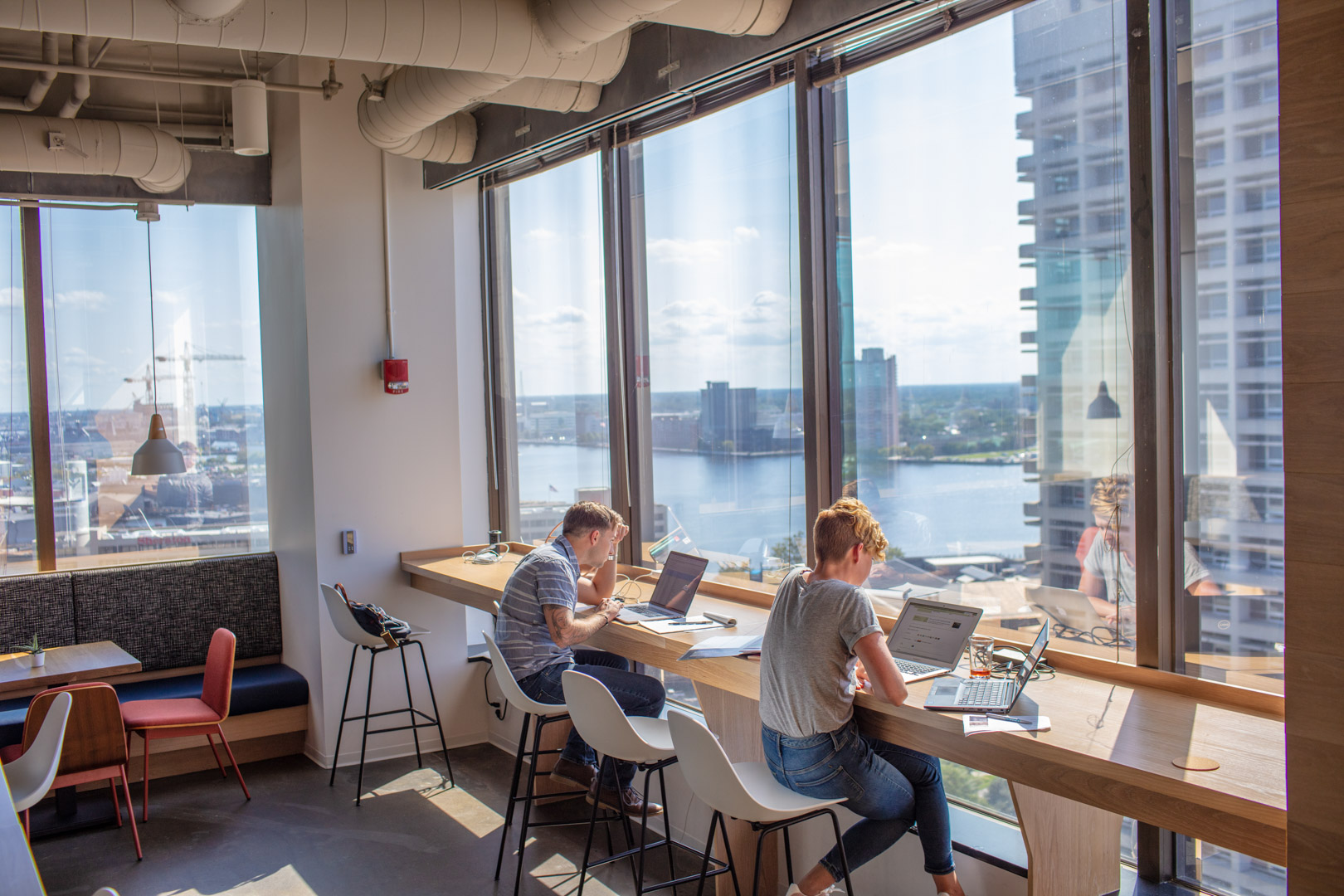 Professionals working at window bar seating with panoramic Norfolk waterfront views at Gather downtown coworking space