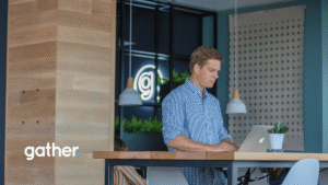Professional working at standing desk in Gather coworking space with modern design, natural wood accents, and branded neon signage.
