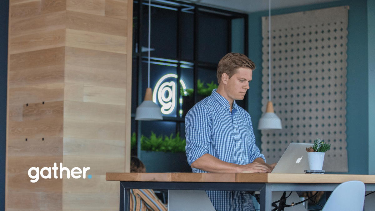 Professional working at standing desk in Gather coworking space with modern design, natural wood accents, and branded neon signage.